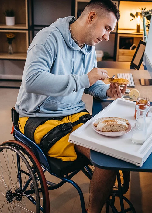 Man in a wheelchair eating breakfast at a desk at home
